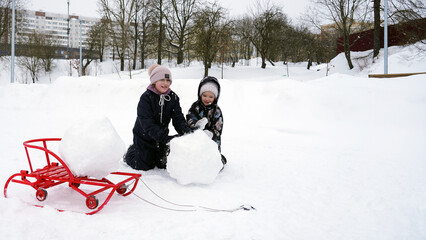 Две девочки лепят снеговика в парке