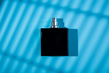 Black bottle of perfume on a blue background. Fragrance presentation with daylight. Trending...