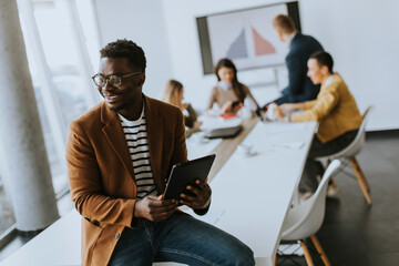 Young African American business man working with digital tablet in front of his coworkers at boardroom