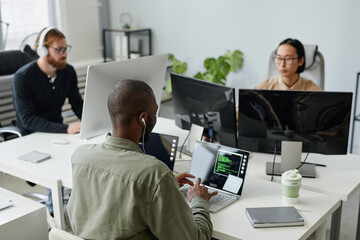 Three young intercultural diversity programmers sitting by desks in front of computers and...