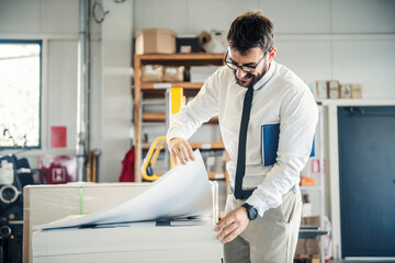 A happy supervisor looking at sheets at printing shop.