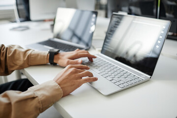 Hands of young contemporary program developer typing on laptop keyboard while sitting by desk in office or bureau