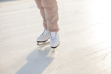 Funny little blonde girl of 7 years old in casual clothes posing on a skating rink in skates. The...