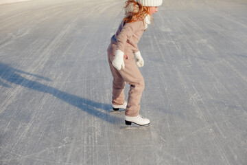 Funny little blonde girl of 7 years old in casual clothes posing on a skating rink in skates. The...
