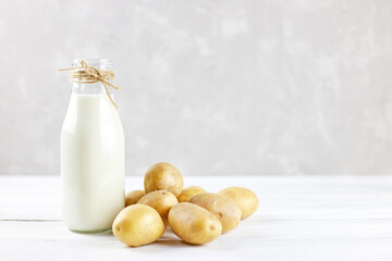 Potato milk in a glass bottle is on the table next to potato tubers. Alternative, vegetable milk is...