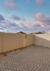 Vertical Puffy clouds at sunset Vinyl fence of a backyard with bricks in herringbone pattern