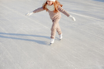 Funny little blonde girl of 7 years old in casual clothes posing on a skating rink in skates. The...