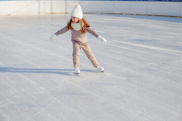 Funny little blonde girl of 7 years old in casual clothes posing on a skating rink in skates. The concept of a child's lifestyle. Layout of the copy space.