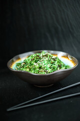 Wakame - Sea Algae Salad beautifully presented in a handmade porcelain bowl, with chopsticks on a dark background