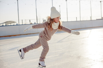 Funny little blonde girl of 7 years old in casual clothes posing on a skating rink in skates. The concept of a child's lifestyle. Layout of the copy space.