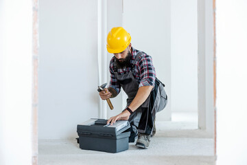 Electrician kneeling in the freshly painted room and taking his tool out of the toolbox.