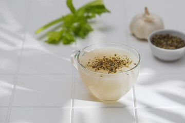 Healthy bone broth with spices in a mug on a white tile with a shadow pattern. 