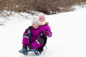 Satisfied happy cheerful children girls sisters siblings sledding down the mountain. Winter activities outside