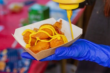 Unrecognizable Asian cook selling street food with fried prawns in mustard sauce at a market in Beijing (China).