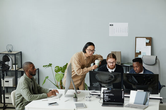 Group of young contemporary program developers gathered in front of computer monitors for discussion of coded data