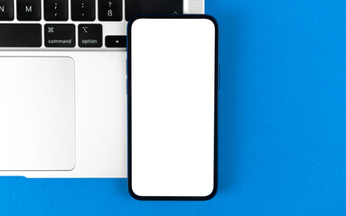 Top view mockup. Smartphone with blank white screen, flat lay blue background with laptop. Minimal workspace, modern laptop, copy space photo