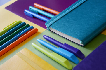 Fototapeta premium Bright notepads and colored pens on a background of colored paper. writing accessories. Corporate gifts for office employees. Sunny mood for work.