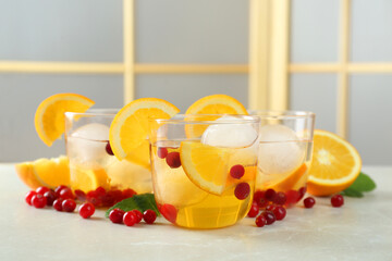 Delicious cocktails with orange, cranberries and ice balls on light grey marble table