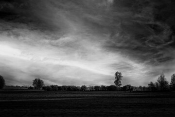dark landscape in black and white with field, trees in distance and dramatic cloudy sky.