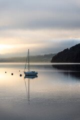 Sailing boat under dramatic sunset sky on Loch Tay Lake at sunset, Kenmore, Perthshire, Highlands of Scotland, United Kingdom, Europe