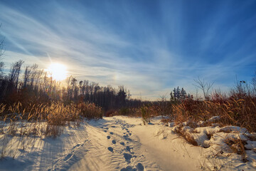 Winter landscape, sunset in the mountains. Clear footprints in the snow. A clear sunny day ends, the sun hides behind the trees of the forest