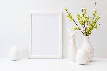 Home interior with easter decor. Mockup with a white frame and willow branches in a vase, easter eggs on a light background