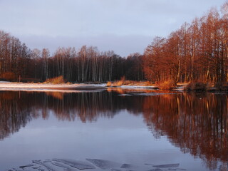 winter landscape by the water golden hour bare trees, river ice and first snow