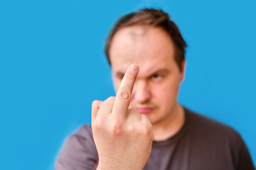 Portrait of disheveled adult man with fucking gesture, blue studio background