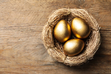 Nest with golden eggs on wooden table, top view. Space for text
