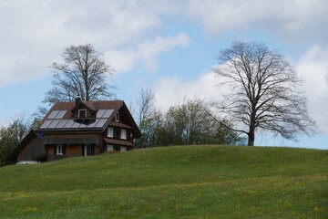 Obraz premium Wooden house with solar panels on the roof. Lonely wooden house in Swiss countryside equipped with modern technology for production of electricity from renewable sources. Copy space available. 
