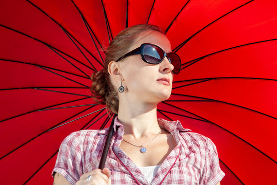 Mujer rubia con gafas de sol negras y sombrilla roja