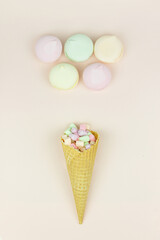Waffle horn with colored marshmallow looks like macaroons on a pink pastel background.