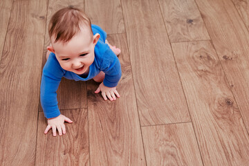 Happy baby toddler crawls on a wooden laminate. Funny child on the parquet in the home living room, aged 6-11 months