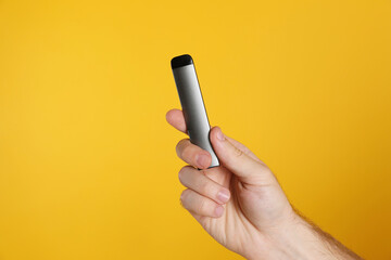 Man holding electronic cigarette on yellow background, closeup