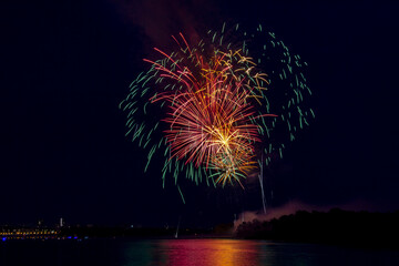 Festive fireworks over the river of a big city. Volley to the right of the river.