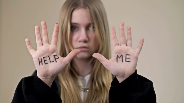 Portrait of a frustrated teenage girl showing her palms with the inscription HELP ME.