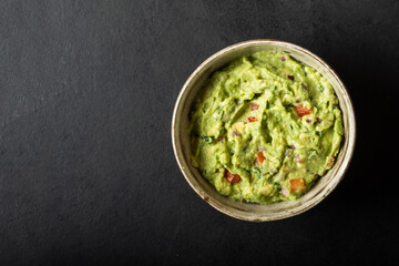 Traditional Mexican Guacamole sauce made from avocado. lime, red onion, tomatoes, cilantro on a black background.