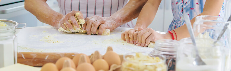 Child and grandmother in the kitchen bakes prepares the dough in the kitchen. Selective focus.