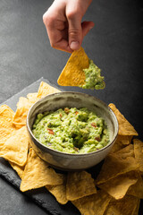 Young man hand is picking some guacamole dip with nachos chip. Healthy Vegan, Vegetables food.