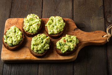 Sandwiches with guacamole sauce on a cutting board over old wooden background.