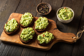 Sandwiches with guacamole sauce on a cutting board over old wooden background.