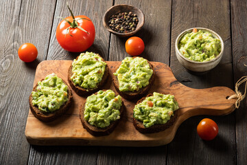Sandwiches with guacamole sauce on a cutting board over old wooden background.