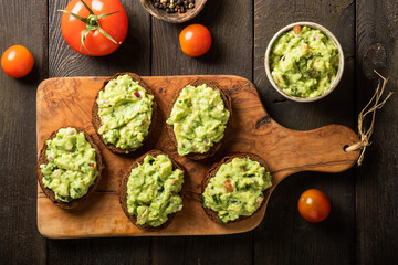 Sandwiches with guacamole sauce on a cutting board over old wooden background.