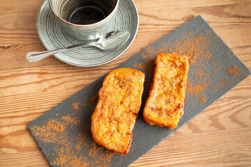 merienda con torrijas hechas  con pan, leche ,huevos y canela , en mesa de madera y caza para el café