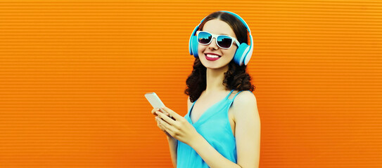 Portrait of happy smiling young woman in headphones listening to music with smartphone on orange...