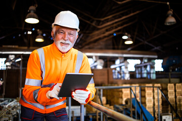 Factory employee standing by production machines and checking manufacture results on tablet...