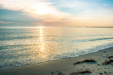 Calm ocean waters and sand reflect beautiful, colorful summer sunset with the reflection of the sun across the water