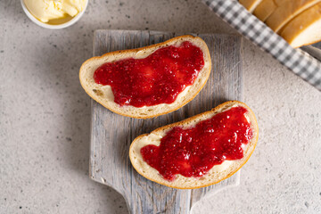 White bread slices with butter and raspberry jam on it, greens on wooden board, organic country sweet sandwich, homemade dessert. Copy space.