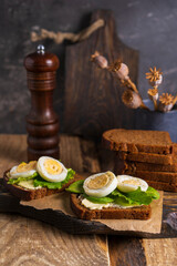 Black whole grain sliced bread with butter, salad leaves  and boiled eggs on wooden rustic table. Country, organic dietic opened sandwich. Copy space. Dark backgroound.