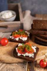 Black whole grain sliced bread with cottage cheese, tomatoes and dill on wooden rustic table. Country, organic dietic opened sandwich. Copy space. 